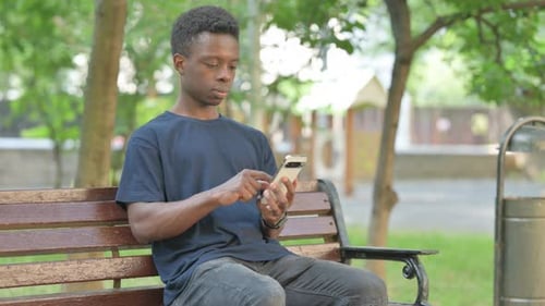 African American Man Typing on Phone on a Park Bench