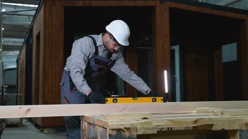 Ouvrier du bâtiment vérifiant le niveau de la poutre en bois avec Spirit Level dans l'atelier