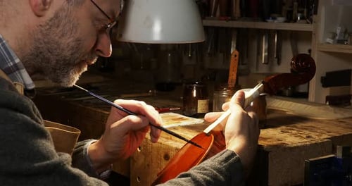 Close up of italian maker carefully applying varnish on a new handcrafted violin in his workshop