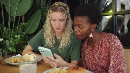 Two Diverse Friends Sharing Content on a Smartphone in a Restaurant