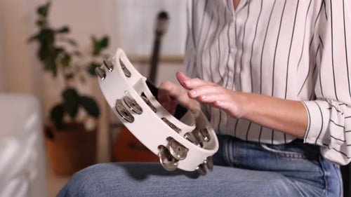 Woman playing tambourine at home, closeup view