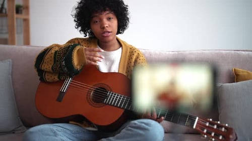 Young Woman Sits with Guitar Recording Video