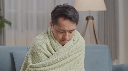Gros plan d'un homme asiatique malade avec une couverture ayant froid sur le canapé dans le salon à la maison
