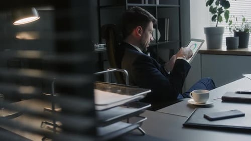 Businessman Examining Financial Charts on Tablet at Office Workplace