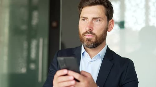 Businessman in formal suit is using smartphone at workplace in business office. Worker reads