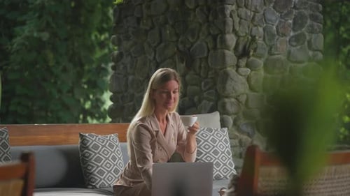 Focused business woman working on laptop at Bali resort lounge while drinking coffee