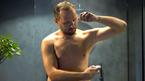Man Spray Deodorant on Armpit and Chest in Bathroom Alone