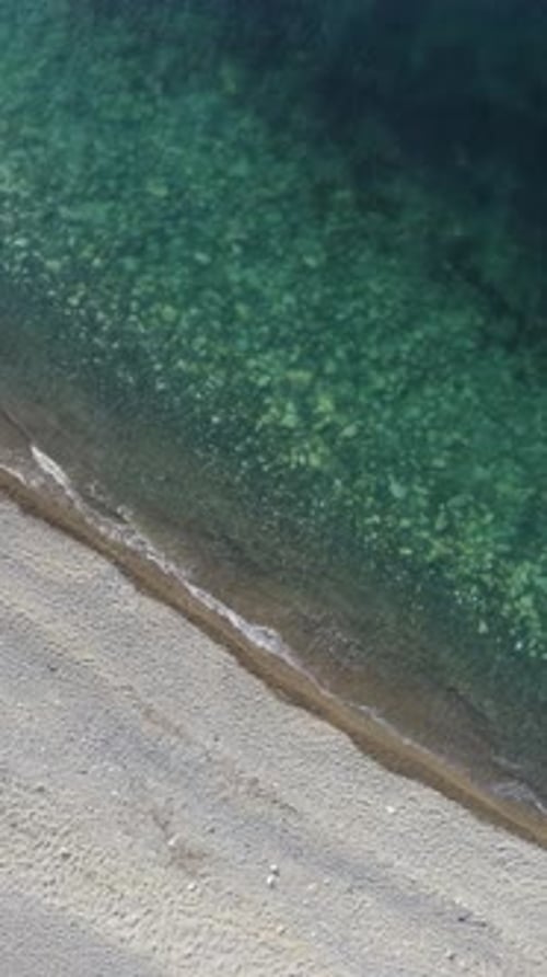 Aerial Vertical View of Beach with Wave Caressing Shore Sun Glare Small Waves on the Water Surface