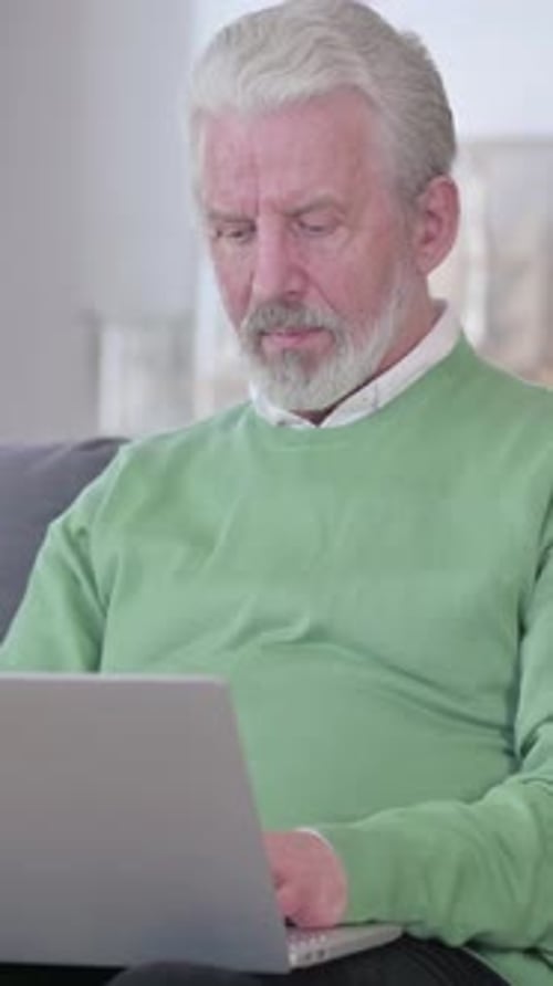 Senior Man Smiling Using a Laptop at Home