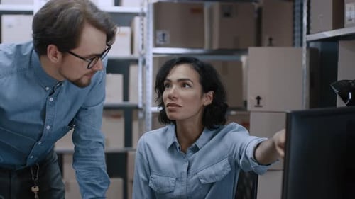 Male and Female Warehouse Inventory Managers Talking, Using Personal Computer and Checking Stock. I