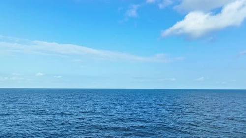 Aerial view over the blue sea with wave, blue sky and white clouds. 4K.