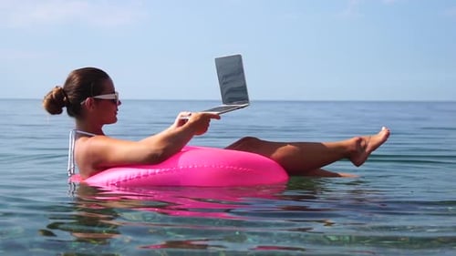 Woman Freelancer Works on Laptop Swimming in Sea on Pink Inflatable Ring Happy Tourist in Sunglasses