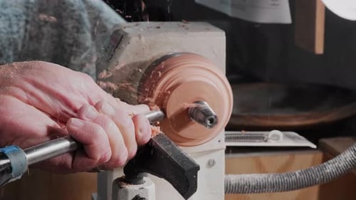 Old man using a lathe and chisel to cut away wood and release a metal grommet