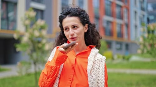 Woman Speaking into Phone Outdoors in Urban Setting