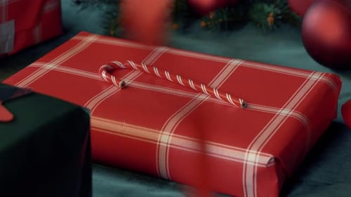 woman wrapping Christmas gifts on a table, with red boxes and a green tablecloth