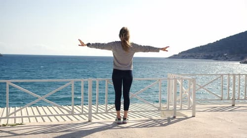 Girl Stand on Embankment with Hands to Sides with Sea or Ocean with Mountains in Background