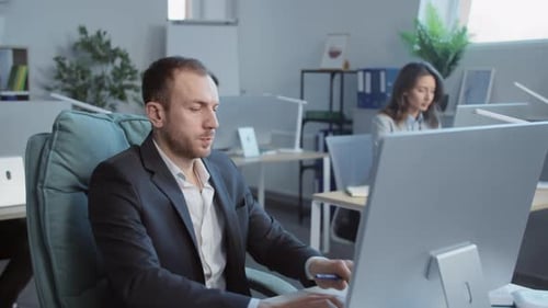 Footage of Tired Office Worker in Black Suit Sitting at Desk and Using Computer in Comfortable