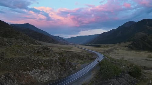 Aerial View of a Valley with a River and Road Surrounded By Mountains at Sunset