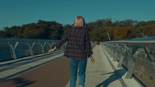 Rear View of Col Trendy Woman in Headphones Riding on Inline Skates Outdoors