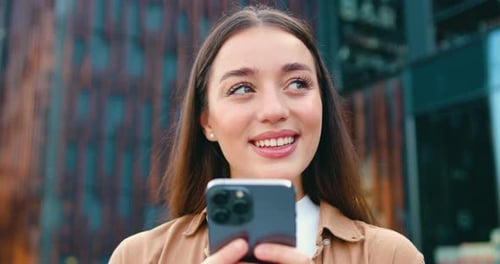 Close-up of satisfied young woman face with long hair and white teeth looking at mobile phone