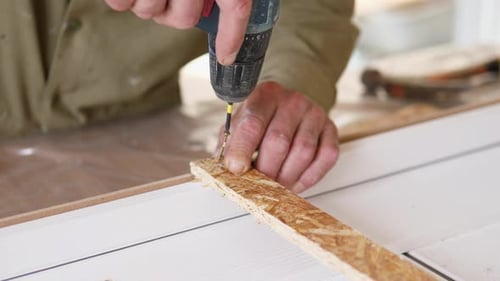Séquence d'assemblage de meubles avec les mains du travailleur perçant et stabilisant la bande d'aggloméré sur fond blanc