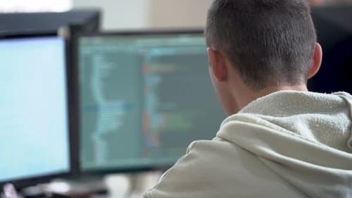 Homem trabalhando no computador, visão traseira. Um programador olha para a tela de um computador․