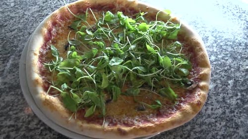 Slow motion shot of a freshly cooked pizza being topped with fresh basil and tomatoes