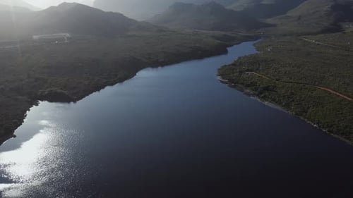 Aerial view of a wide river mouth tracking forward and tilting up to reveal mountain range at sunset