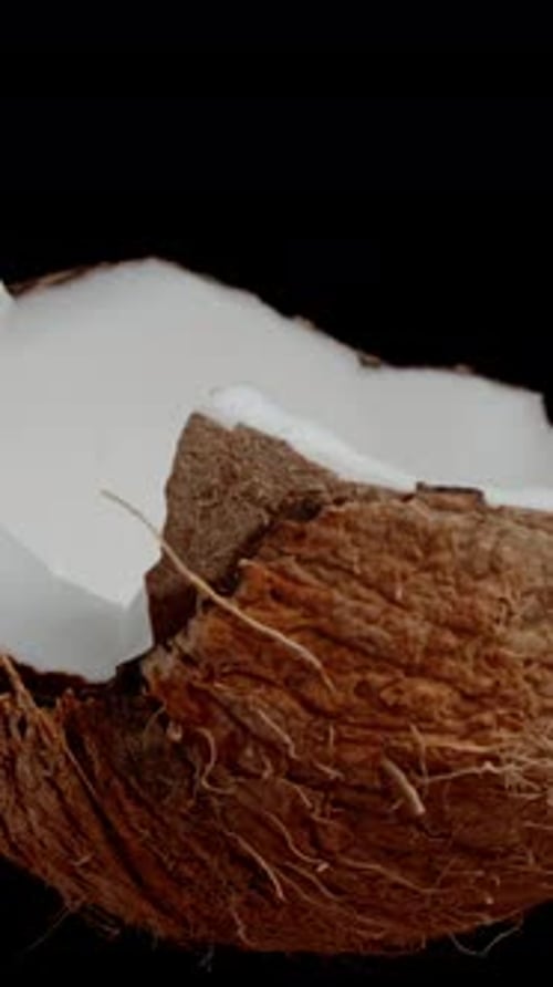 Vertical video. Half of a cracked coconut, looped video on an isolated black background.