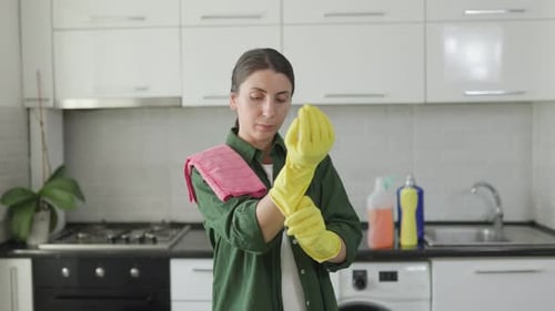 Caucasian Woman in a Modern Kitchen Putting on Yellow Gloves for Housework