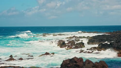 Slow motion static close up shot of rough ocean waves crushing against the volcanic rocky coastline.