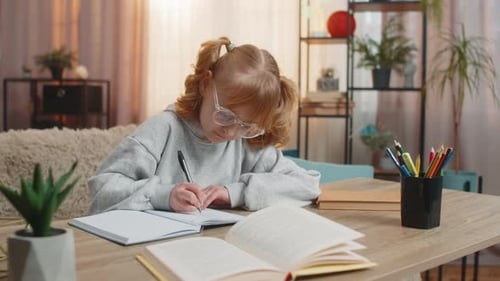 Young Schoolgirl Sitting at Table on Sofa Doing Homework with Notebook Celebrating Solution with Joy