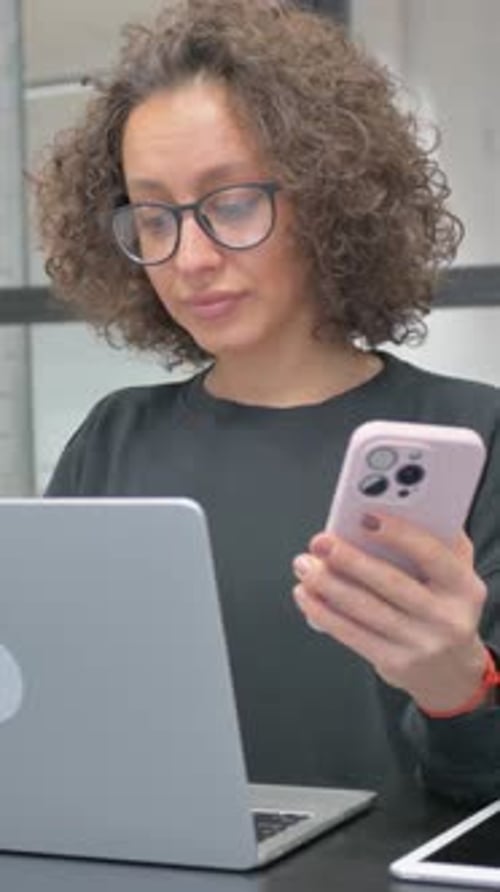 Woman Using Laptop and Phone in Office