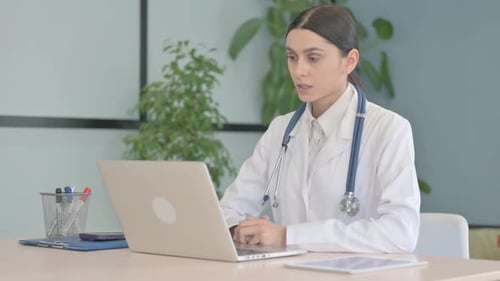 Online Video Chat by Young Female Doctor on Laptop in Clinic