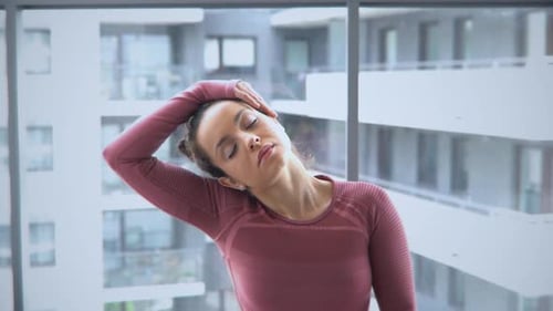 Woman Stretching Neck Before Window in Home Setting