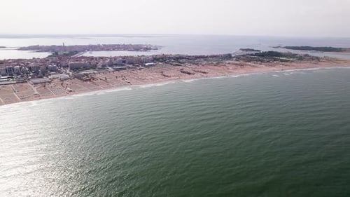Cinematic aerial drone footage moving to the right along a beach and coastline with a coastal city