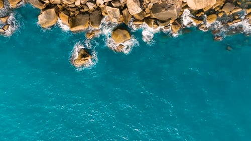 Waves foam and rock. Aerial view of crashing waves on rocky shore.