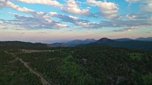 Aerial view of a glowing sunset behind mountain peaks casting shadows over a forested valley below