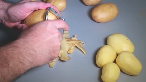 Man Peeling Potatoes with Vegetable Peeler Close Up