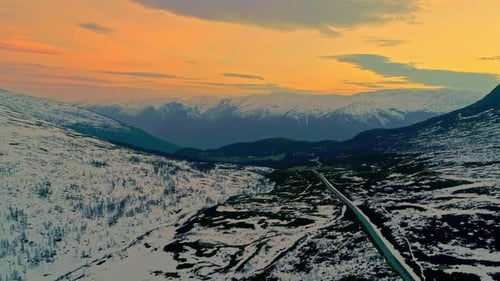 Aerial drone backward moving shot over a snow covered country road on mountain plateau surrounded by