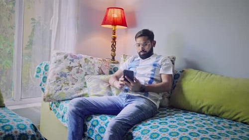 Young Adult Using Smartphone on Sofa Indoors