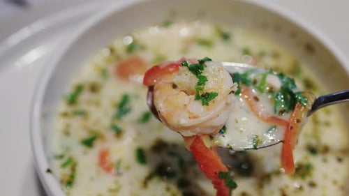 Primer plano de un camarón recogido con una cuchara de una sopa con hierbas y verduras