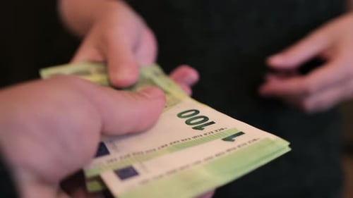 Man's hand reaches for the money of woman who reluctantly gives it away, close up.