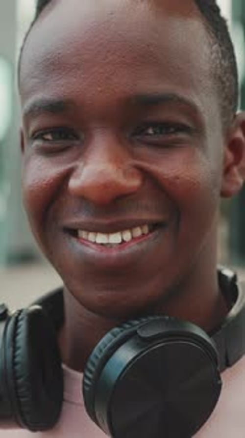 Clouse up, smiling young student stands outside of university in headphones
