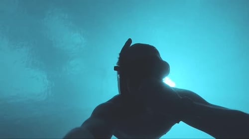 Slow motion shot of man free diving underwater, silhouette of man underwater.