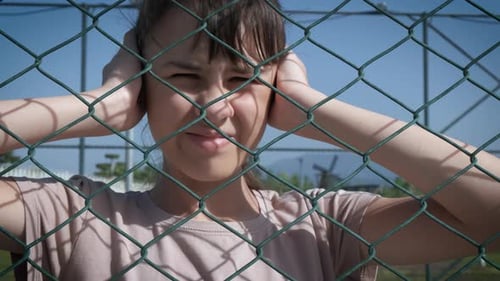 Teen Outside Fence Covers Her Ears