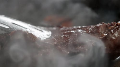 Steak Sizzling on a Hot Grill with Tongs