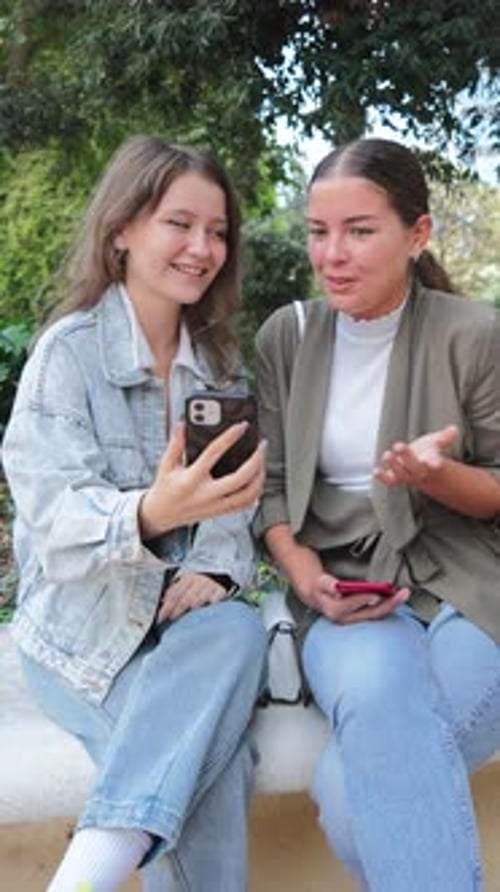 Two Young Women Viewing Smartphone Outdoors in Casual Setting