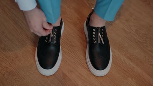 Man Zips Up Leather Shoes on Wooden Floor
