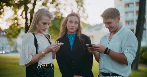 Three Young Adults Using Smartphones in City Park